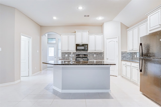 kitchen with black appliances, dark stone countertops, white cabinets, and an island with sink