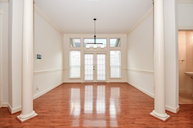 unfurnished dining area with wood-type flooring, a chandelier, ornate columns, and ornamental molding