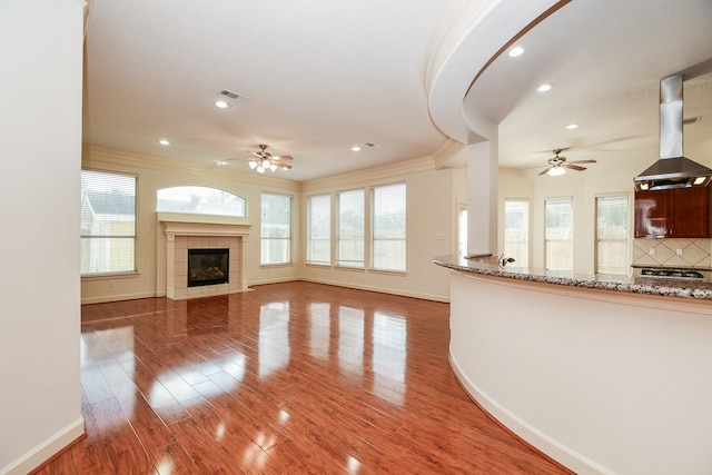 unfurnished living room with ceiling fan, a tile fireplace, a healthy amount of sunlight, and dark hardwood / wood-style floors