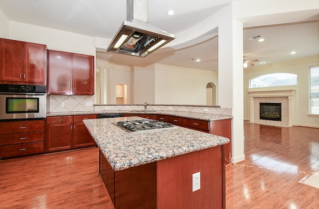 kitchen featuring stainless steel appliances, range hood, crown molding, a center island, and light hardwood / wood-style flooring