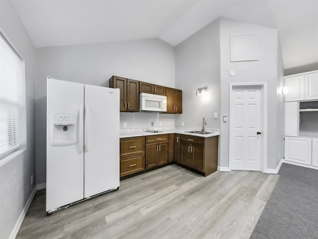 kitchen with dark brown cabinets, sink, vaulted ceiling, light wood-type flooring, and white appliances