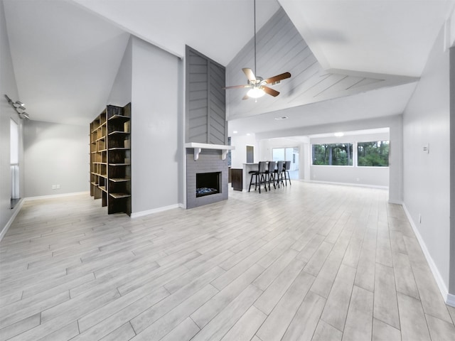 unfurnished living room featuring a brick fireplace, ceiling fan, beam ceiling, high vaulted ceiling, and light hardwood / wood-style flooring