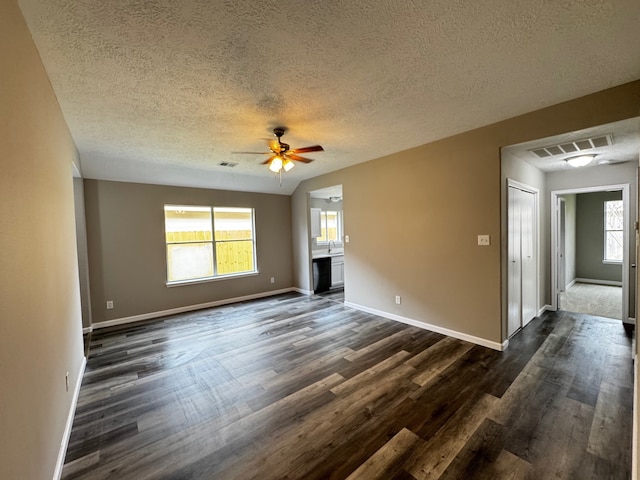 unfurnished living room with a textured ceiling, a healthy amount of sunlight, dark wood-type flooring, and ceiling fan