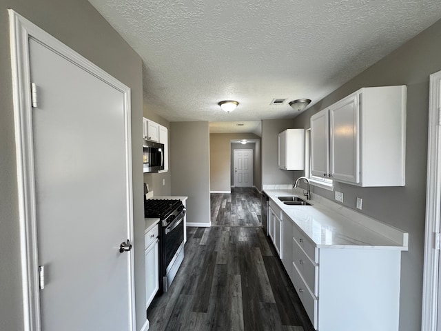 kitchen with appliances with stainless steel finishes, white cabinetry, a textured ceiling, dark wood-type flooring, and sink