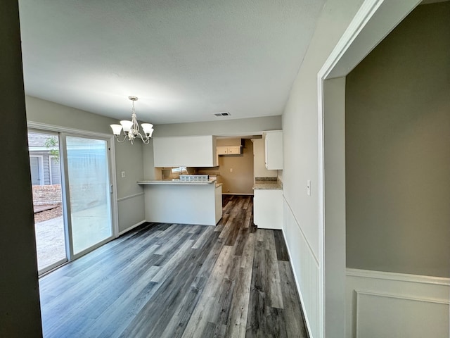 kitchen with dark hardwood / wood-style flooring, kitchen peninsula, decorative light fixtures, white cabinets, and an inviting chandelier