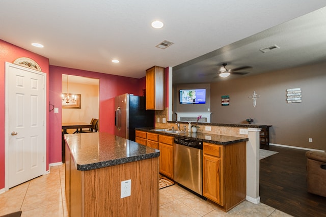 kitchen with ceiling fan with notable chandelier, a center island, kitchen peninsula, stainless steel appliances, and light tile patterned floors