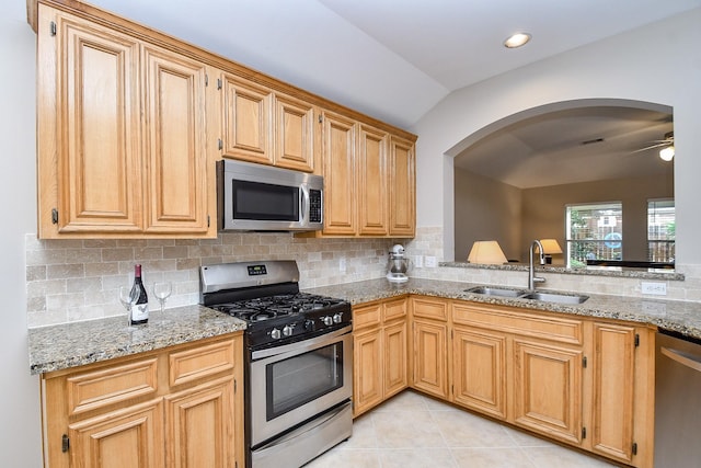 kitchen with appliances with stainless steel finishes, backsplash, light stone counters, sink, and light tile patterned flooring