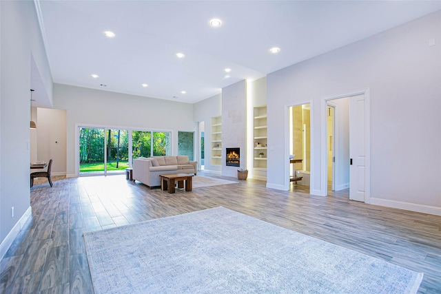 unfurnished living room featuring built in shelves, a large fireplace, and hardwood / wood-style flooring