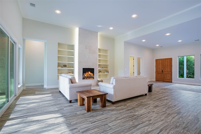 living room featuring light wood-type flooring, a large fireplace, and built in features