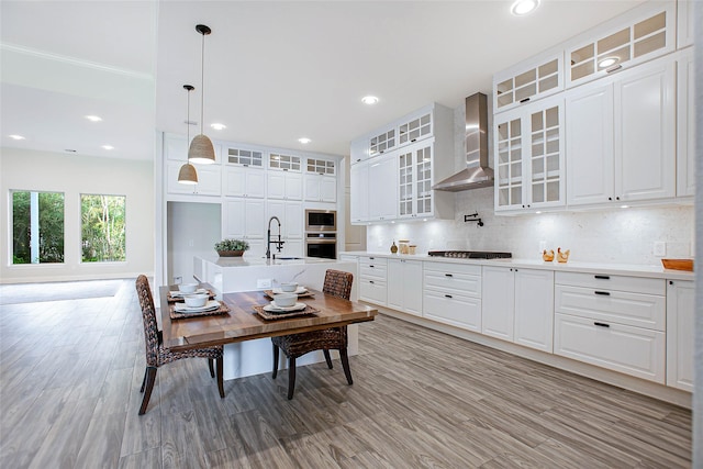 kitchen featuring white cabinets, wall chimney exhaust hood, stainless steel appliances, and decorative light fixtures