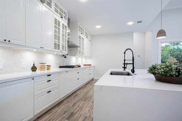 kitchen with sink, wall chimney range hood, light hardwood / wood-style flooring, pendant lighting, and white cabinets