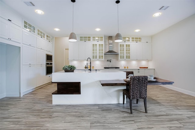 kitchen with sink, wall chimney exhaust hood, an island with sink, pendant lighting, and appliances with stainless steel finishes