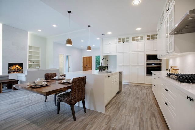 kitchen with sink, white cabinetry, a kitchen island with sink, and range hood