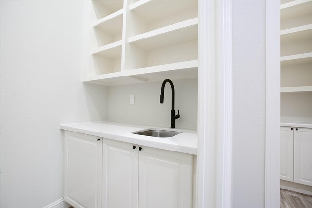 bar featuring light hardwood / wood-style flooring, white cabinetry, and sink