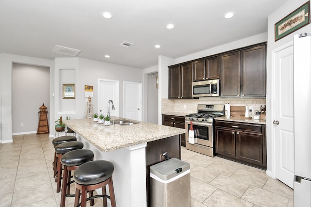 kitchen with tasteful backsplash, dark brown cabinets, appliances with stainless steel finishes, a kitchen island with sink, and sink