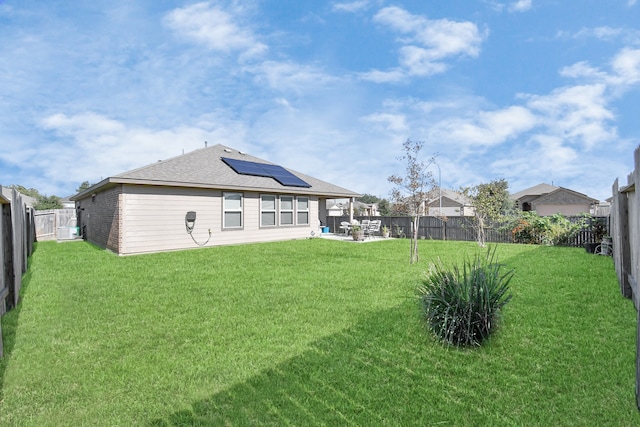 back of property with solar panels and a yard