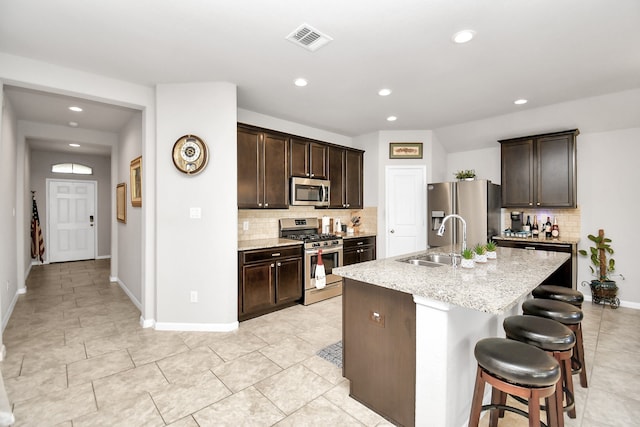 kitchen featuring stainless steel appliances, decorative backsplash, sink, and an island with sink