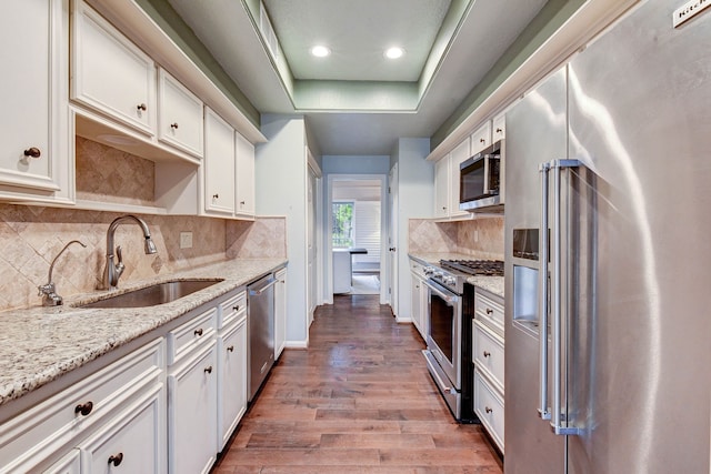 kitchen with premium appliances, wood-type flooring, sink, white cabinetry, and light stone counters