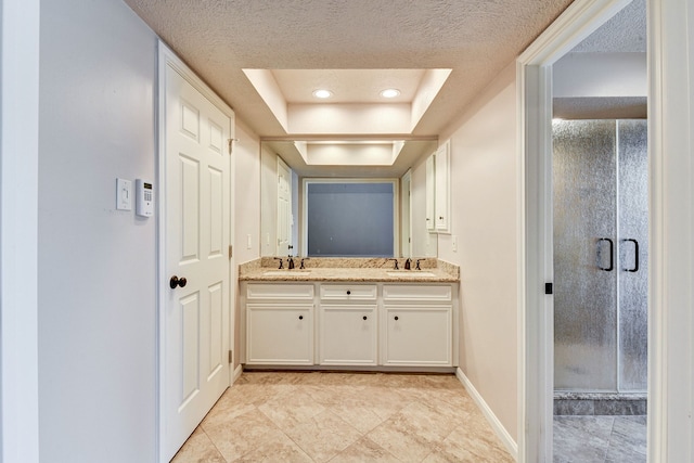 bathroom with vanity, a textured ceiling, a shower with shower door, and a raised ceiling