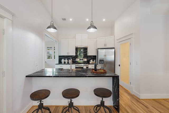 kitchen with white cabinetry, stainless steel appliances, decorative light fixtures, and light wood-type flooring