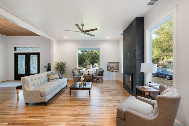 living room featuring light hardwood / wood-style floors, a healthy amount of sunlight, a tile fireplace, and ceiling fan