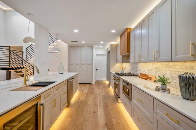 kitchen featuring beverage cooler, stainless steel appliances, sink, light hardwood / wood-style floors, and decorative light fixtures