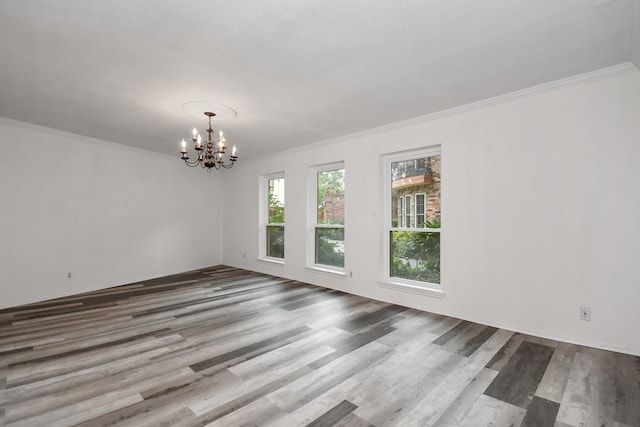 empty room featuring hardwood / wood-style flooring, ornamental molding, and an inviting chandelier