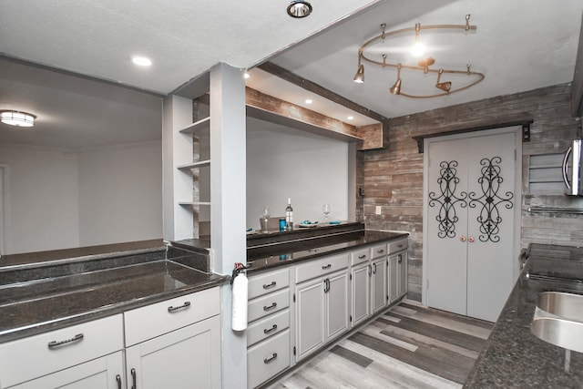 kitchen with white cabinetry, dark stone countertops, wooden walls, and sink