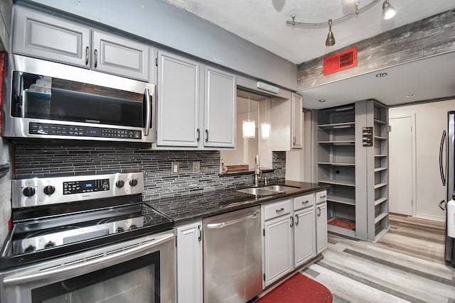 kitchen with decorative backsplash, stainless steel appliances, sink, decorative light fixtures, and light hardwood / wood-style flooring