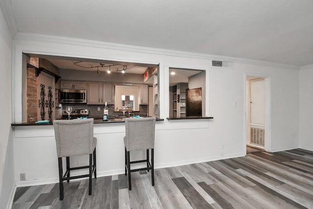 kitchen featuring hardwood / wood-style floors, crown molding, decorative backsplash, a kitchen bar, and stainless steel appliances