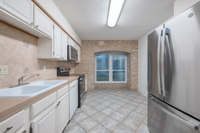 kitchen featuring brick wall, sink, appliances with stainless steel finishes, light tile patterned floors, and white cabinets