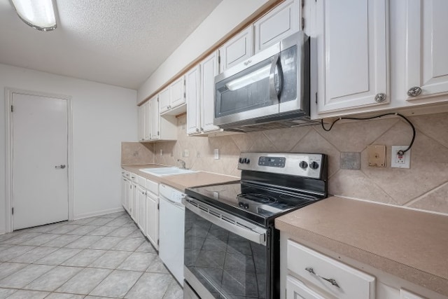 kitchen with tasteful backsplash, stainless steel appliances, white cabinetry, light tile patterned floors, and sink