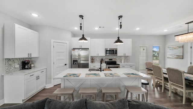 kitchen featuring appliances with stainless steel finishes, white cabinetry, a kitchen island with sink, and hanging light fixtures