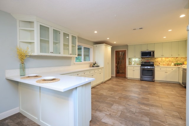 kitchen with stainless steel appliances, kitchen peninsula, a breakfast bar area, backsplash, and white cabinetry