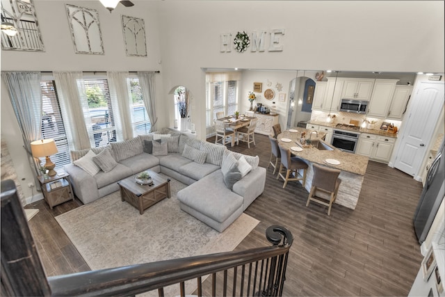 living room with ceiling fan, a towering ceiling, sink, and dark hardwood / wood-style floors