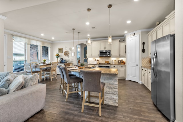 kitchen featuring appliances with stainless steel finishes, dark hardwood / wood-style floors, decorative light fixtures, and a center island with sink