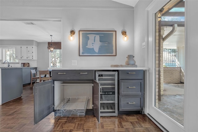 kitchen featuring dark parquet flooring, sink, gray cabinetry, hanging light fixtures, and beverage cooler