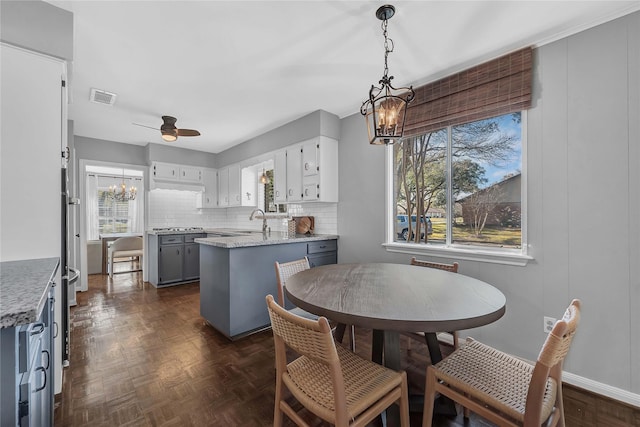 dining space with dark parquet flooring, sink, and ceiling fan with notable chandelier