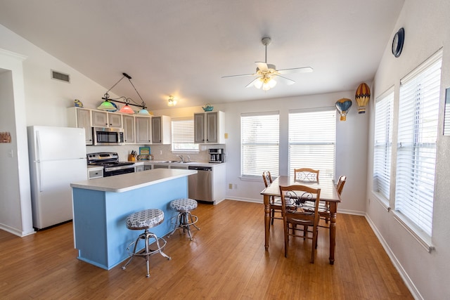 kitchen with appliances with stainless steel finishes, light wood-type flooring, a kitchen bar, a center island, and lofted ceiling