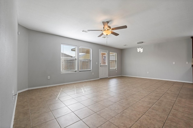 spare room featuring ceiling fan with notable chandelier, plenty of natural light, and light tile patterned floors