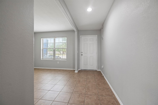 interior space with a textured wall, light tile patterned flooring, and baseboards