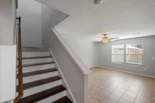 stairway featuring visible vents, a ceiling fan, a textured ceiling, baseboards, and tile patterned floors