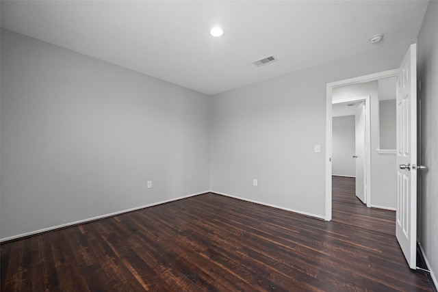 spare room with dark wood-type flooring, visible vents, and baseboards