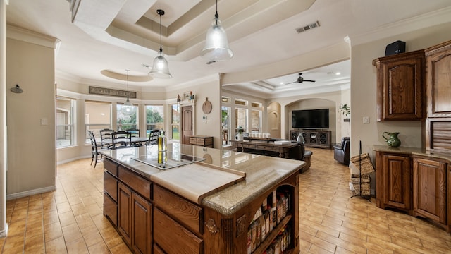 kitchen with a raised ceiling, crown molding, a kitchen island, and ceiling fan