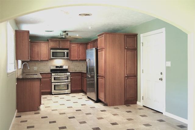 kitchen with backsplash, dark stone counters, sink, ceiling fan, and stainless steel appliances