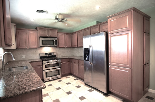 kitchen featuring backsplash, dark stone counters, a textured ceiling, stainless steel appliances, and sink