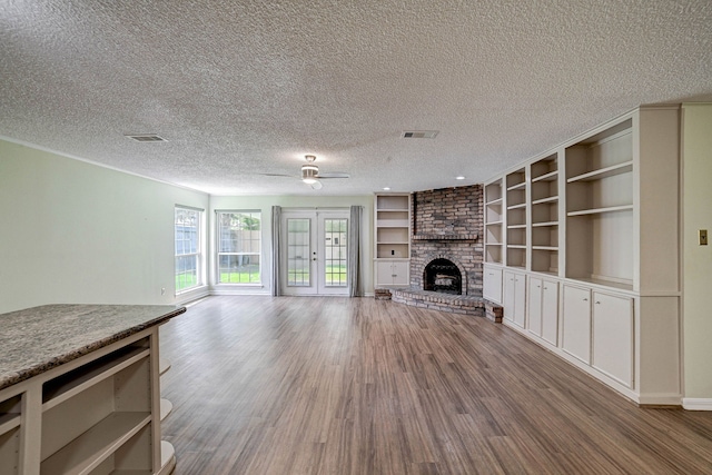 unfurnished living room with french doors, light hardwood / wood-style floors, a textured ceiling, and a fireplace