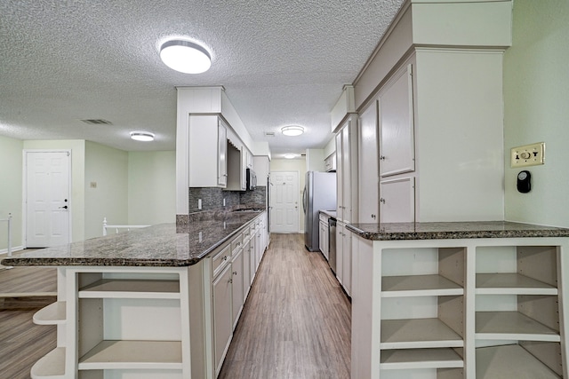 kitchen with a textured ceiling, white cabinetry, stainless steel appliances, decorative backsplash, and light hardwood / wood-style flooring