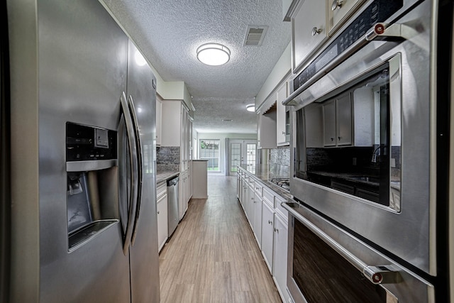 kitchen featuring appliances with stainless steel finishes, light wood-type flooring, backsplash, a textured ceiling, and white cabinets