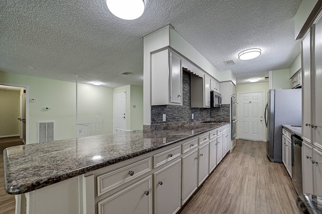 kitchen featuring decorative backsplash, stainless steel appliances, white cabinetry, a textured ceiling, and light hardwood / wood-style floors